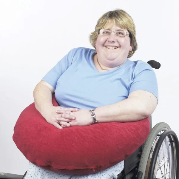 A smiling woman in a wheelchair with a red bean bag supporting her arms and hands as they are crossed